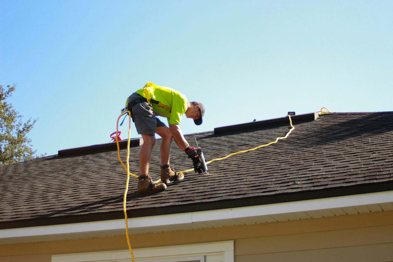 A roofer fastening asphalt shingles on a residential roof