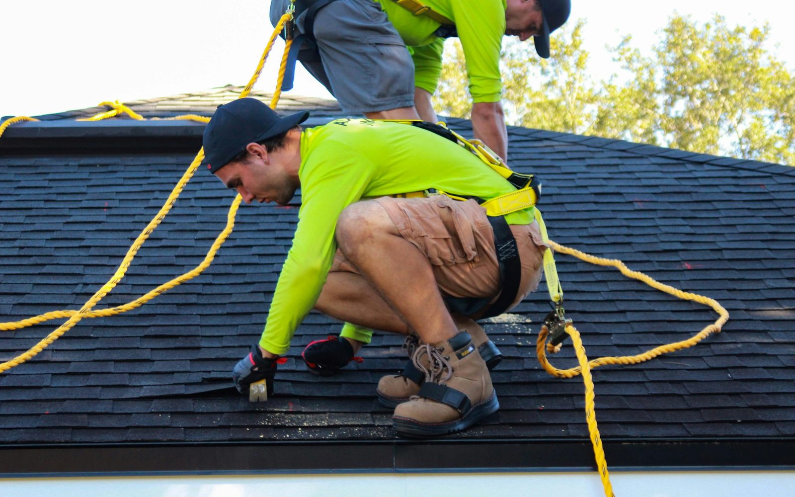 Roofer in a safety harness working on an asphalt shingle roof