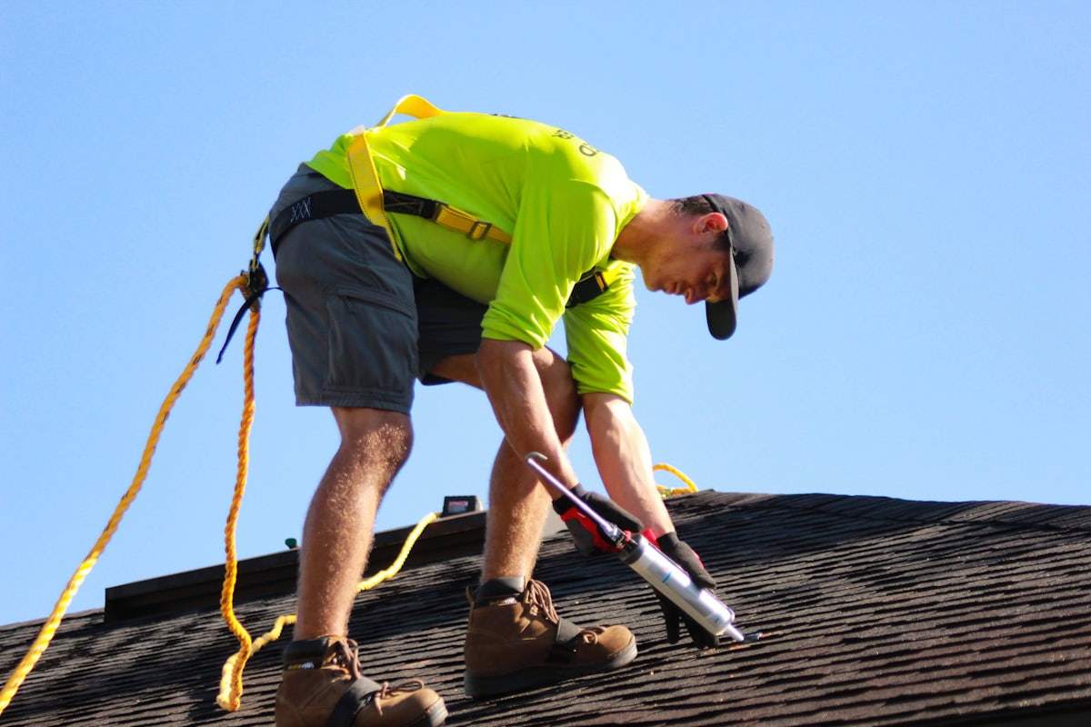 Roofer applying sealant along a shingle roof