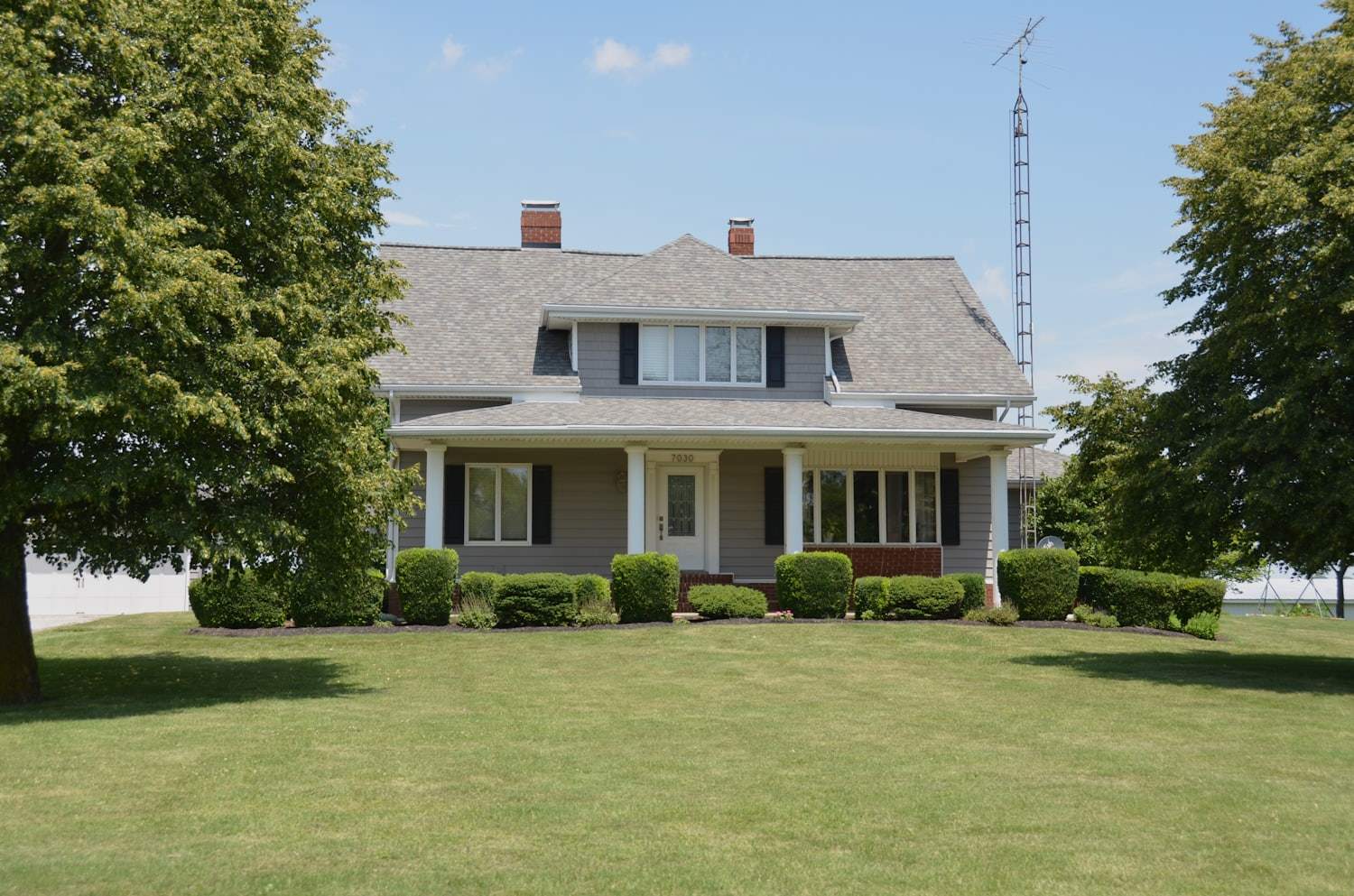 A grey two-story home with a covered front porch and a wide green lawn