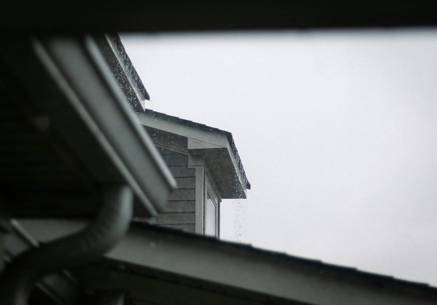 Rain running off a roofline past a gutter and downspout